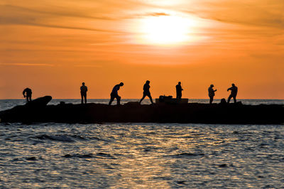 Silhouette of people on sea against sky during sunset