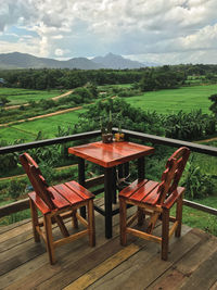 Empty chairs and table by trees against sky