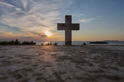 View of cross in sea against sky during sunset