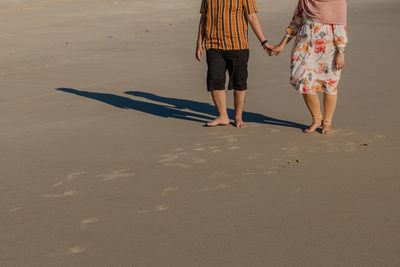 Low section of couple walking on sand at beach