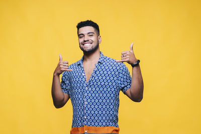 Portrait of smiling young woman standing against yellow background