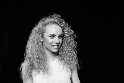 Portrait of smiling woman with curly hair standing against black background