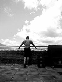 Rear view of shirtless man standing by railing against sky