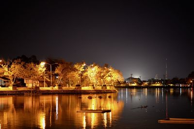 Illuminated city by river against sky at night