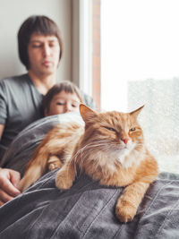Father, son,cute ginger cat sit on window sill.man, toddler, fluffy pet at cozy home while snowfall.
