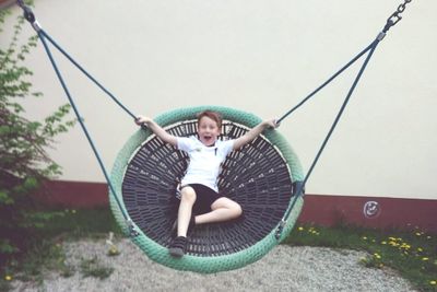 Portrait of playful boy enjoying on swing against wall