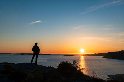 Silhouette man looking at sea against sky during sunset