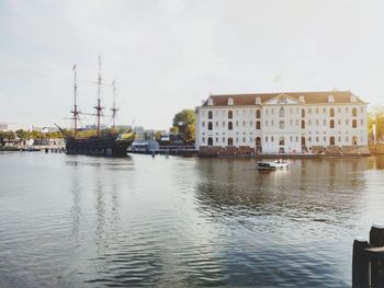 Sailboats in river by buildings against sky