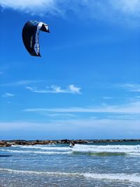 Person paragliding in sea against sky