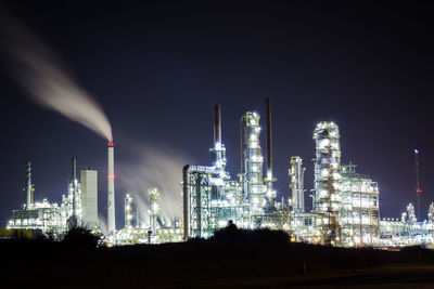 Illuminated factory against sky at night