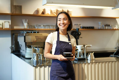 Portrait of smiling young woman standing in kitchen