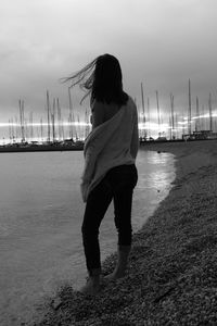 Rear view of woman standing at shore against sky during sunset