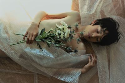 High angle view of naked boy holding flowers while lying with bubble wrap on floor