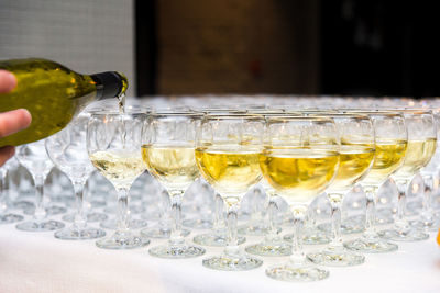 Glasses are filled with alcoholic beverages, the waiter's hand pours white wine from a bottle