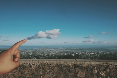 Optical illusion of finger touching cloud in sky