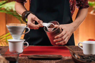 Midsection of woman holding ground coffee at table