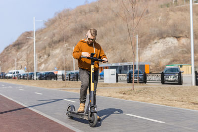 Rear view of man riding push scooter on road
