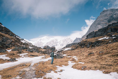 Scenic view of snowcapped mountains with man on rock against sky