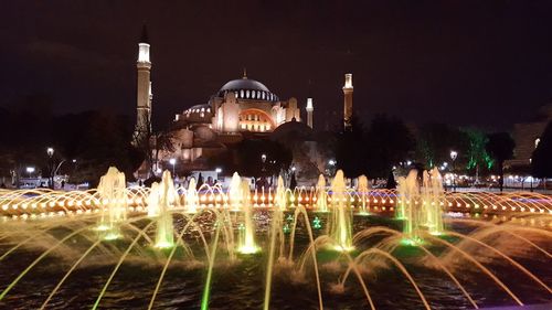 Illuminated fountain and church against sky at night