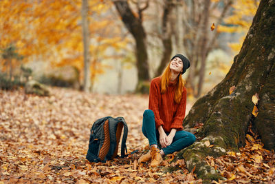 Young woman sitting on tree trunk during autumn