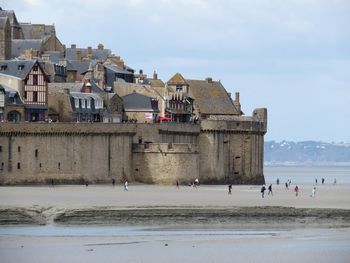 People on beach by buildings against sky