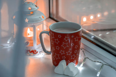 Winter still life with mug with hot drink, two marshmallow, candle on window. valentine's concept. 