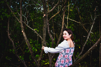 Portrait of young woman standing against trees in forest