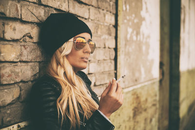 Fashionable young woman wearing jacket standing against brick wall