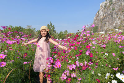 Portrait of smiling young woman standing by pink flowering plants