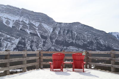 Empty chairs on snowcapped mountain against sky