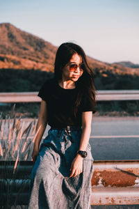 Young woman wearing sunglasses on railing against sky