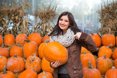 Portrait of a smiling young woman standing by pumpkins