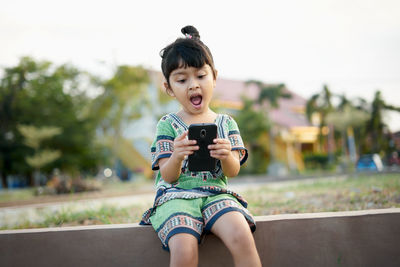 Cheerful girl using mobile phone while sitting outdoors