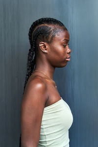 Side view young african american female with long braids wearing tube top and looking away on gray background