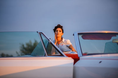 Portrait of woman sitting on car against sky