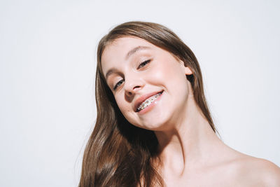 Beauty portrait of girl with fresh skin and long hair, teenager with braces on teeth on white  