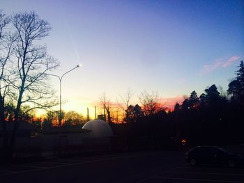 Cars on road by buildings against sky during sunset