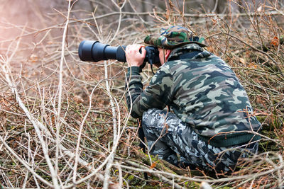 Full length of shirtless man holding camera in forest