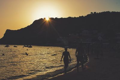 Silhouette people on beach against sky during sunset