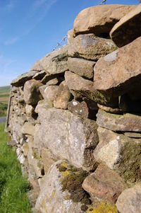 Stone wall by rocks against sky