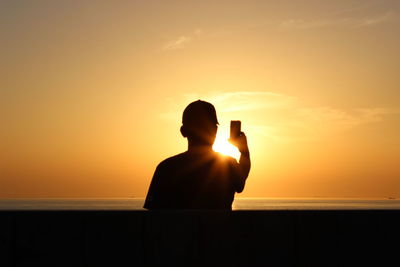Silhouette man sitting by sea against sky during sunset