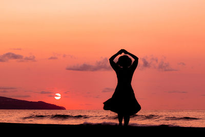 Silhouette woman standing at beach against sky during sunset