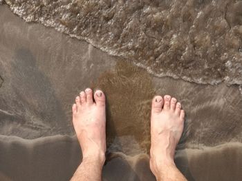 Low section of man relaxing on wet beach