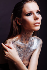Shirtless young woman with silver glitter on her body against black background