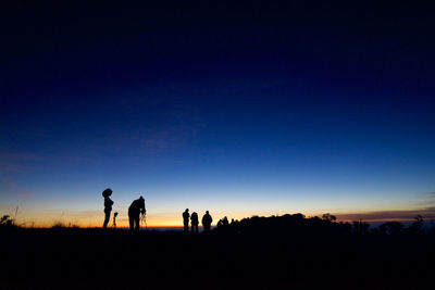 Silhouette people on landscape against sky during sunset