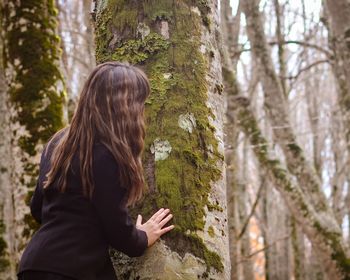 Rear view of young woman standing by tree trunk in forest