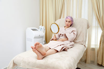 Midsection of woman sitting on bed at home
