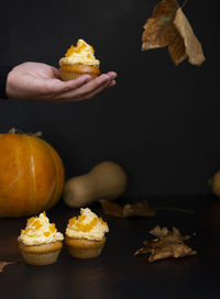 Cropped image of person holding pumpkin on table against black background