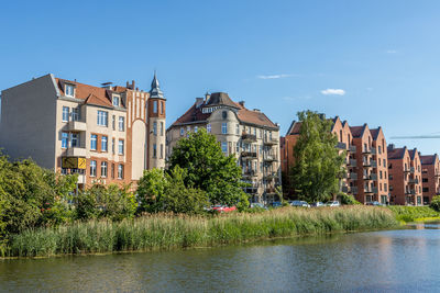 Buildings by river against blue sky