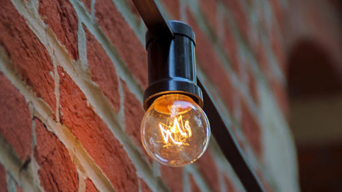 Low angle view of illuminated light bulb on brick wall